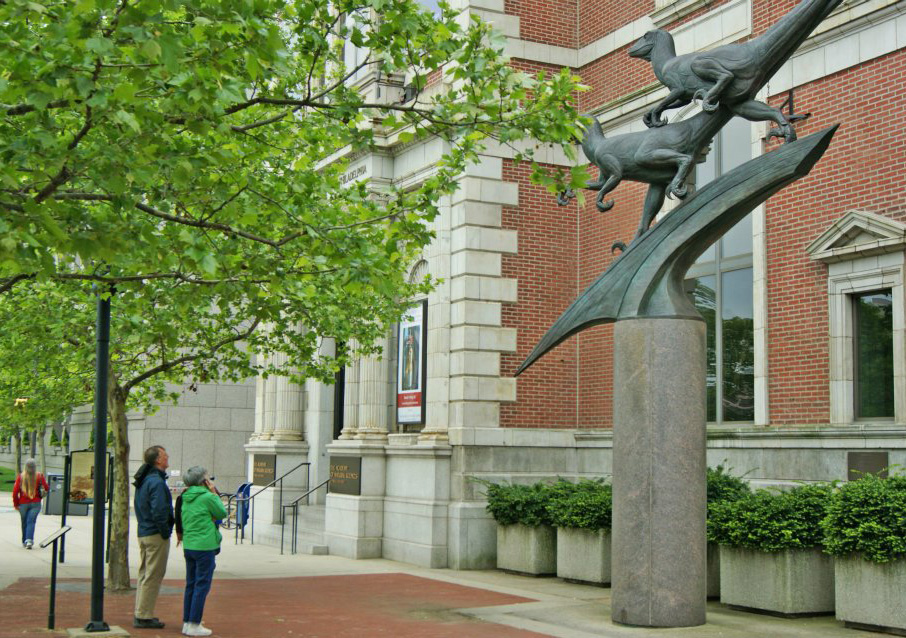 A woman listens to the Museum Without Walls: AUDIO program for “Deinonychus” (stop #11) on her cell phone in front of the Academy of Natural Sciences.