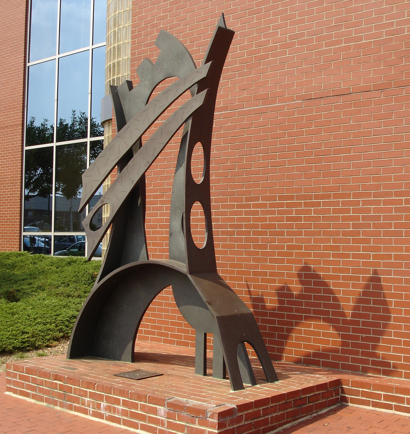 11-foot-tall bronze abstract sculpture, on concrete and brick base, by Philadelphia artist Charles Searles. Sculpture is in front of a red brick wall.