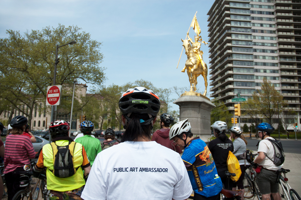 A bike tour led by a public art ambassador stops in front of Emmanuel Frémiet's Joan of Arc