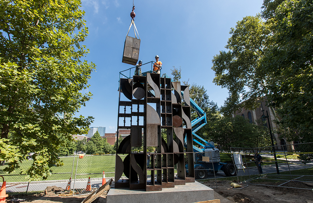 A block of the geometric cort-ten steel sculpture is lowered into place