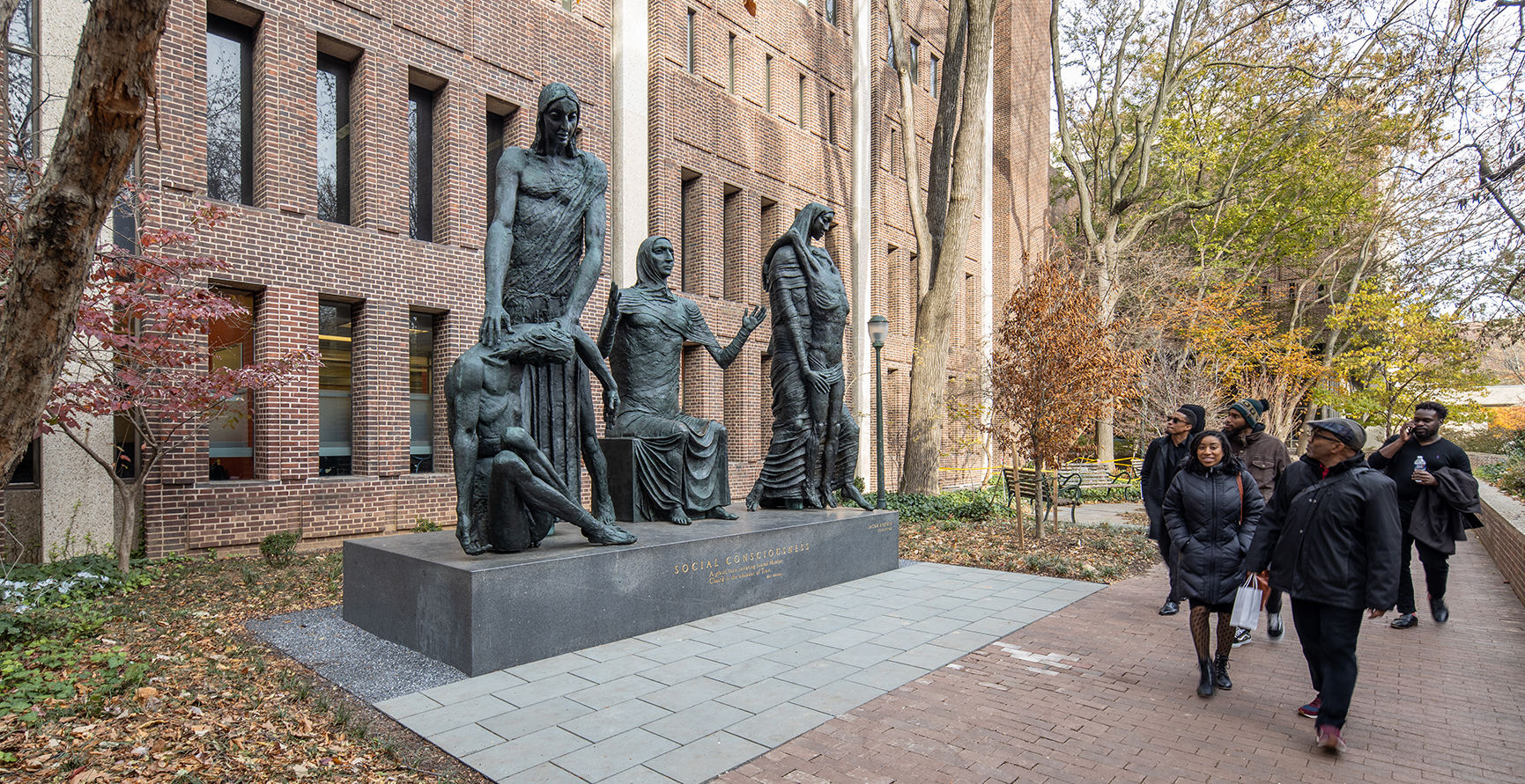 Group of passersby look on at sculpture of four bronze figures in a row