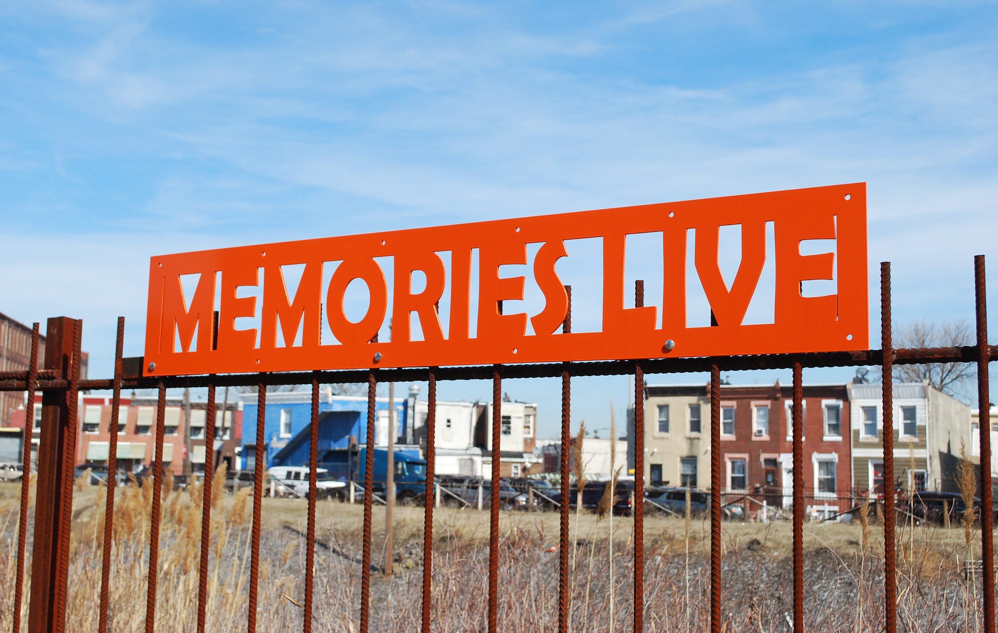Bright orange metal structures, both poetry and sculptures, atop the fence along the Gurney Trail