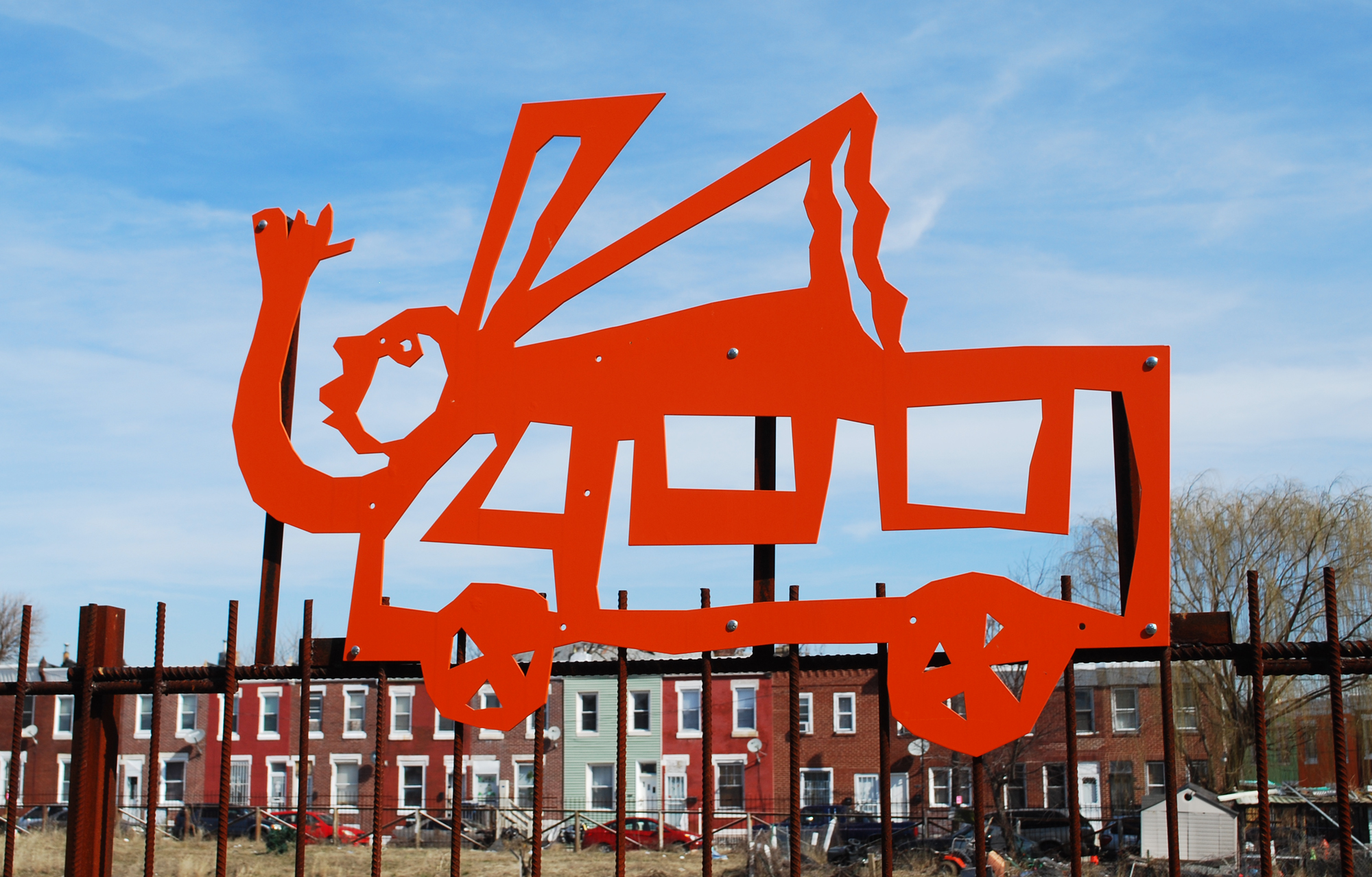 Bright orange metal structures, both poetry and sculptures, atop the fence along the Gurney Trail