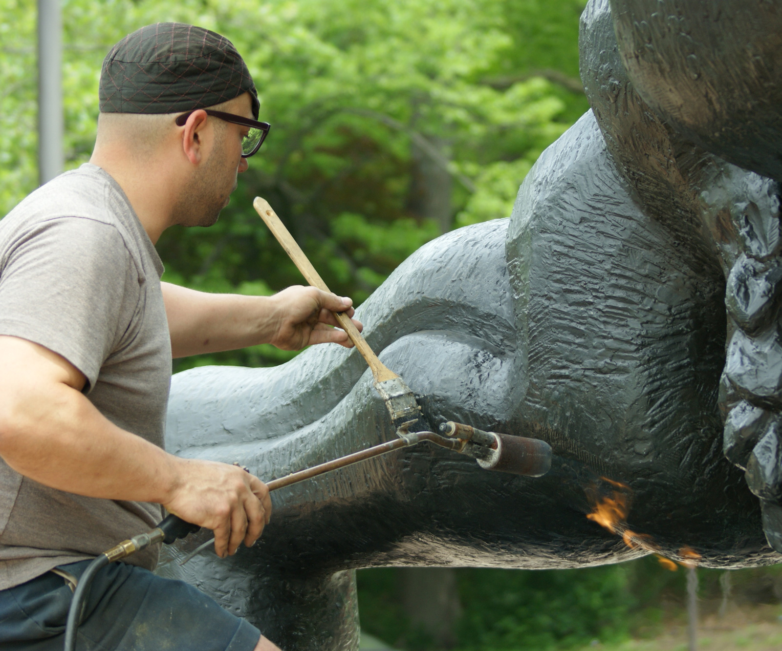 conservator using a brush and blowtorch to apply a wax coating to a bronze Jacques Lipchitz sculpture along Philadelphia's Kelly Drive
